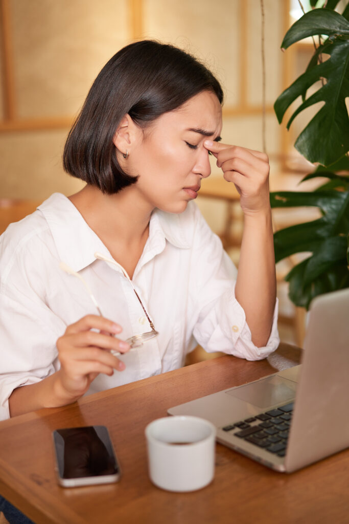 Working woman feeling tired, rubbing eyes after using laptop, having fatigue, sitting in cafe with coffee